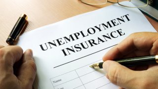 Foto de la mano de alguien sosteniendo un lápiz mientras llena una solicitud de ayuda por desempleo.