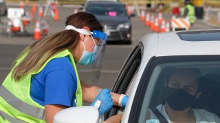 Foto de una mujer colocando una vacuna a una persona sentada en su auto.