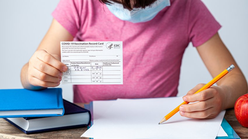 Menor sujetando una tarjeta de vacunación y tomando apuntes en su libreta.