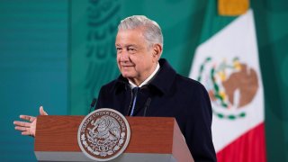 fotografía de un hombre mayor, de cabello cano, que viste un saco negro y está de pie detrás de un atril