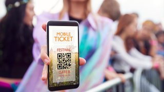 Foto de una persona sujetando un celular que muestra un boleto de entrada a un festival