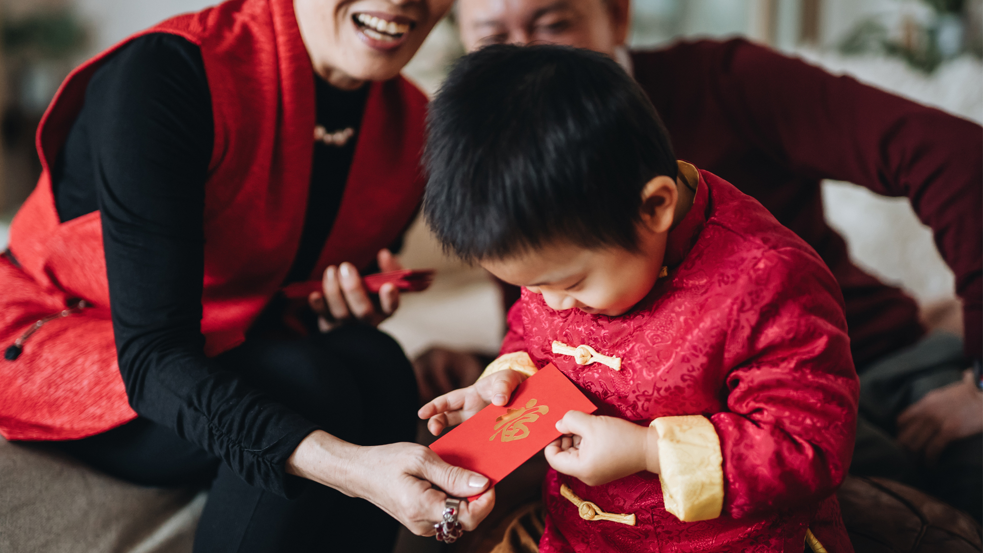 A little boy dressed in a Tang style red jacket receives a red envelope during Lunar New Year