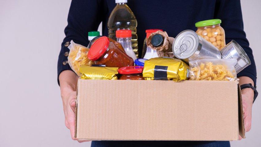 Woman volunteer hands holding food donations box with food grocery products.