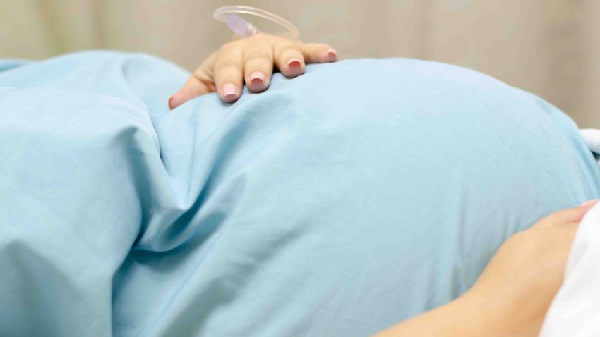 A close up of a women waiting for her scheduled cesarean section where she is holding her pregnant tummy, and you can see a drip in her hand.