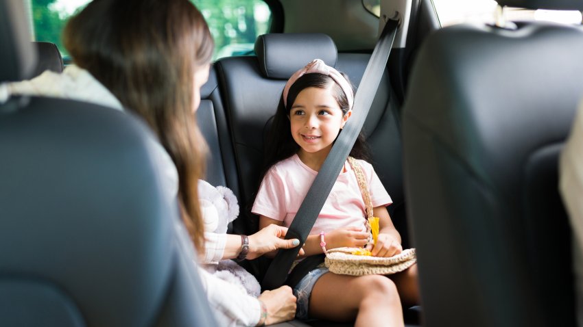 Adorable little girl smiling and looking at her mom while putting their safety seat belt on in the car before starting a family road trip