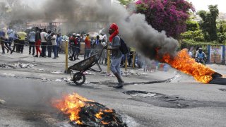 Un hombre empuja una carretilla frente a neumáticos en llamas durante una protesta para exigir la renuncia del primer ministro Ariel Henry, el jueves 7 de marzo de 2024, en Puerto Príncipe, Haití.