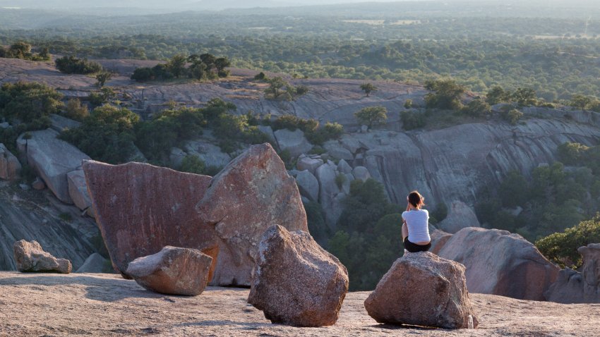 Woman sitting on rock at sunset and Texas Hill Country scenery at Enchanted Rock, large, natural granite outcropping near Austin, Texas.